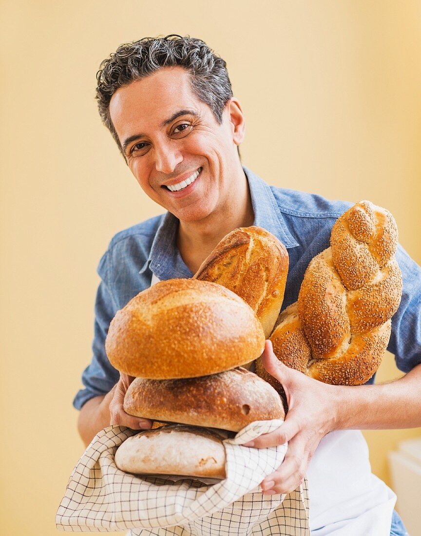 A man in an apron holding assorted freshly baked loaves of bread