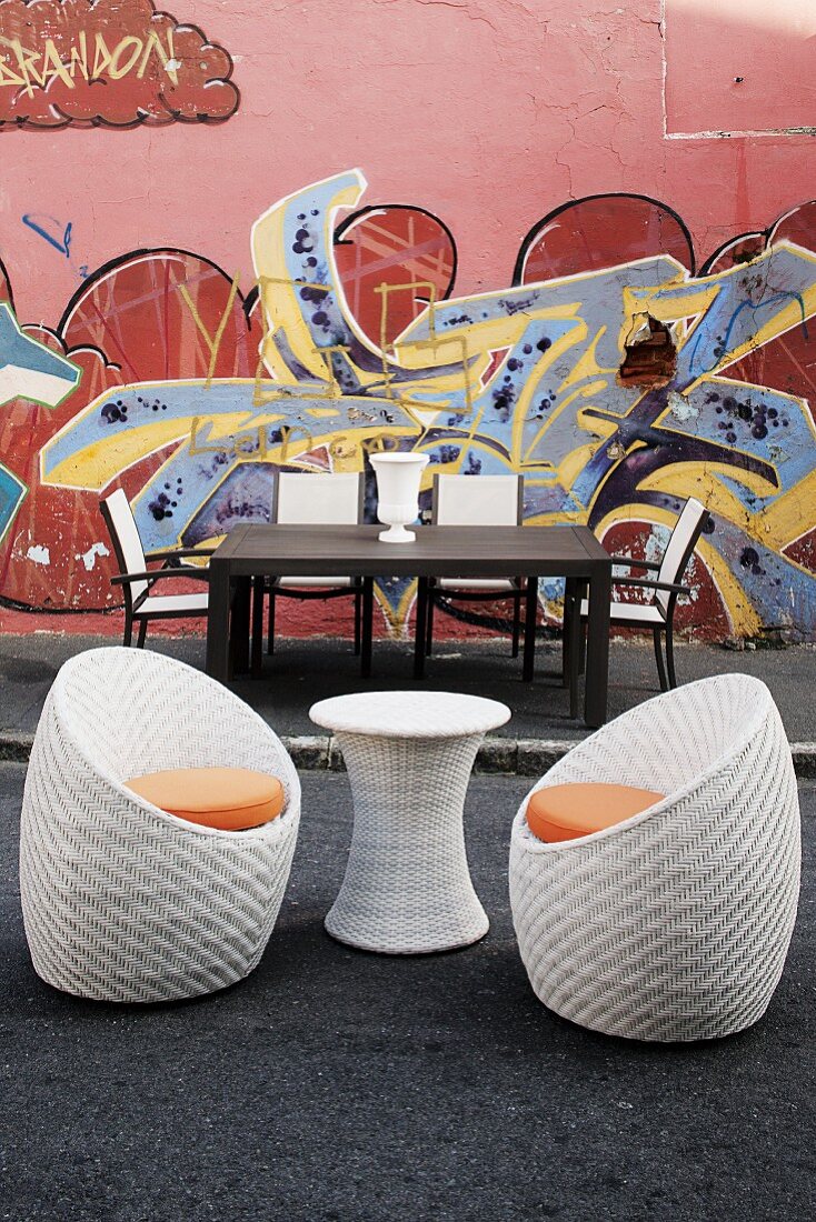 Garden table and chairs and wicker side table with two shell chairs in front of house wall painted with graffiti