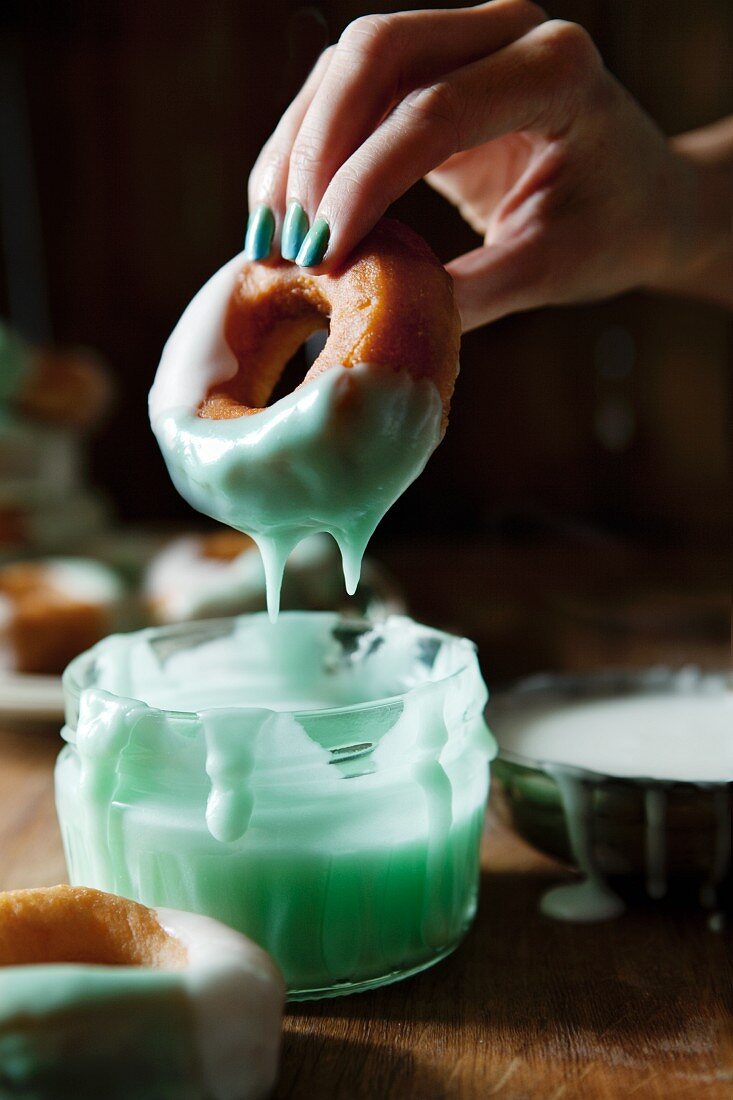 A doughnut being dipped in turquoise icing