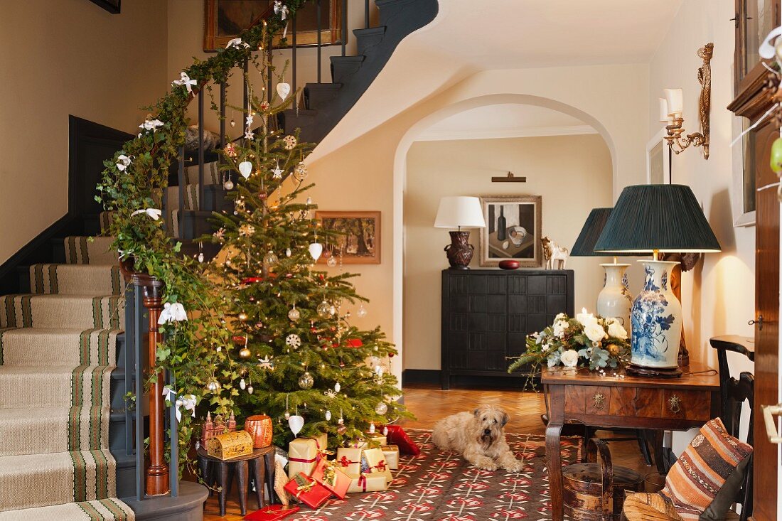 Open-plan foyer of traditional country house with decorated Christmas tree and garland on staircase balustrade