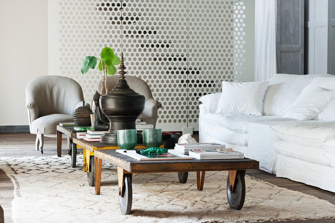 Alte Gepäckwagen als Couchtisch auf marokkanischem Teppich vor weisser Couch und grauen Sesseln