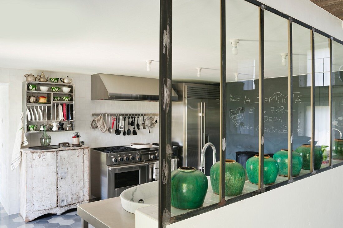 Green ceramic vases on half-height wall in kitchen with vintage cupboard next to stainless steel cooker; blackboard wall in background