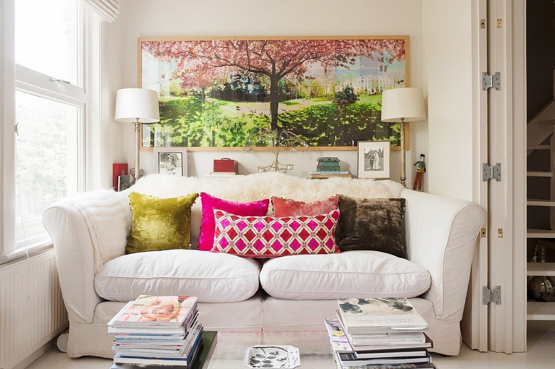 Comfortable sofa with colourful scatter cushions in niche below hand-coloured photograph on wall