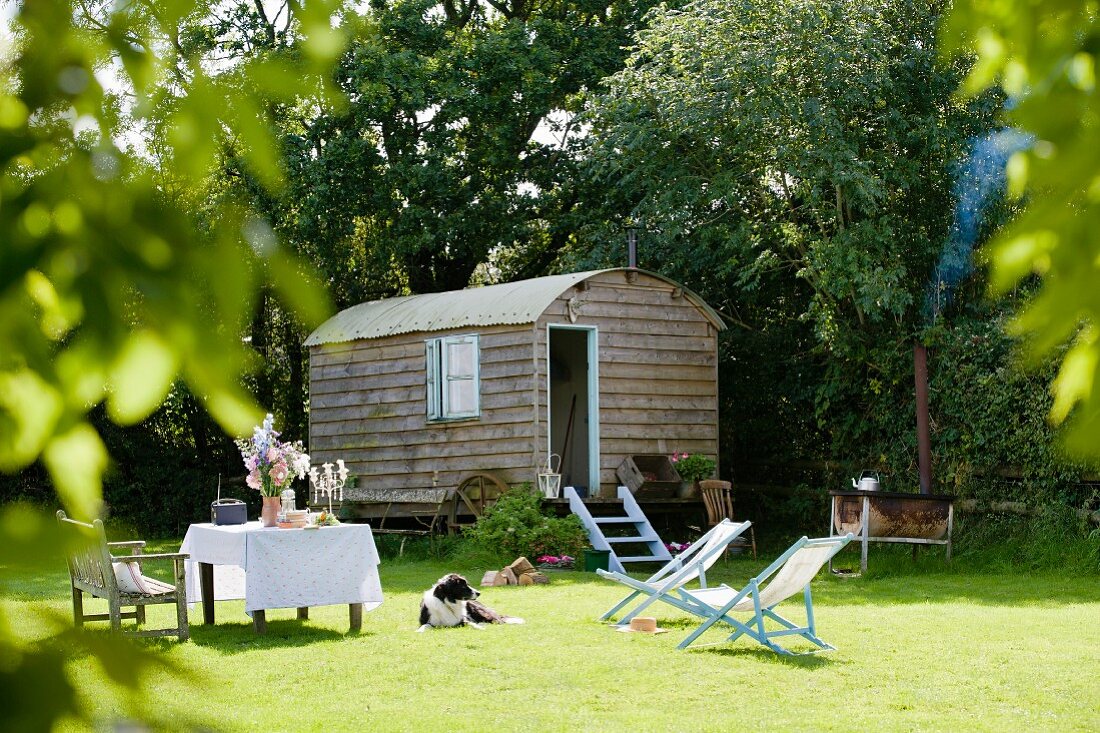 Nostalgic caravan on green lawn with set table and pale blue deckchairs in romantic setting