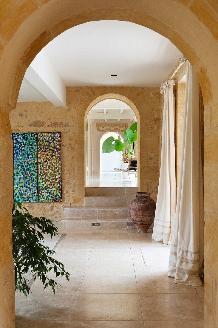 View through row of arched doorways in historical mill in the Dordogne region; painting on stone wall and urn in front of stone steps