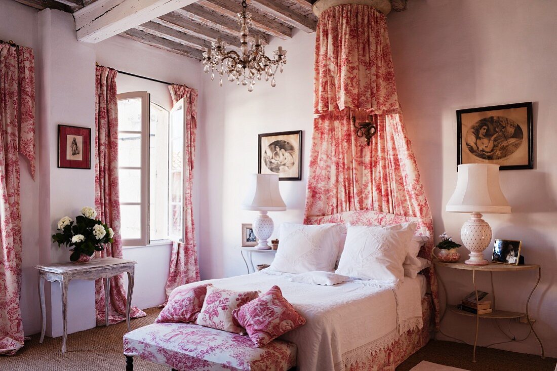 Romantic, shabby-chic bedroom with red and white Toile de jouy fabric curtains, bedroom bench, scatter cushions and canopy