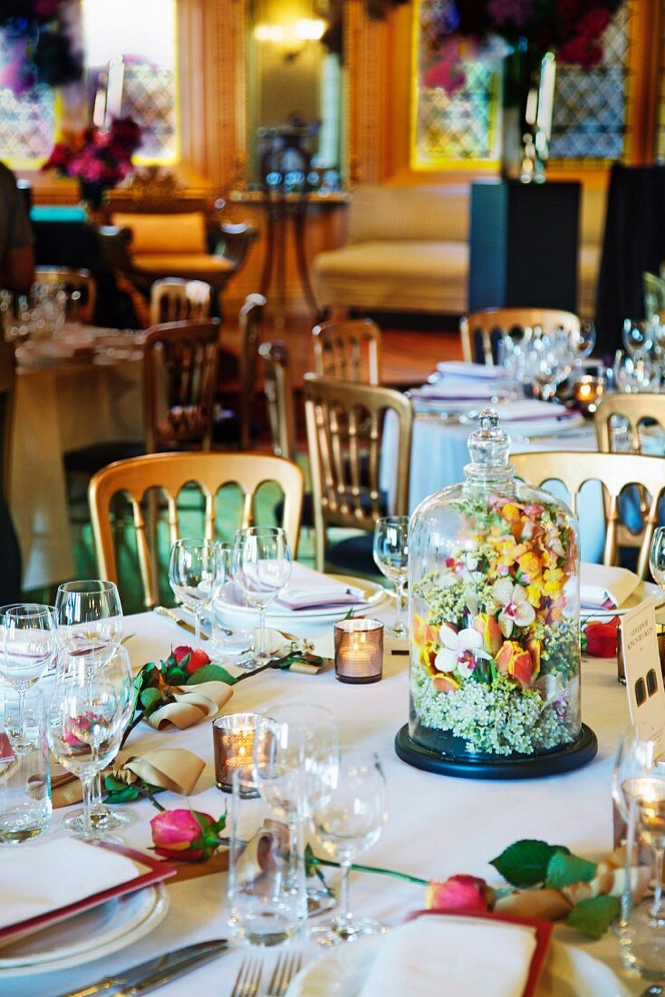 A celebration table with a floral arrangement under a glass cloche