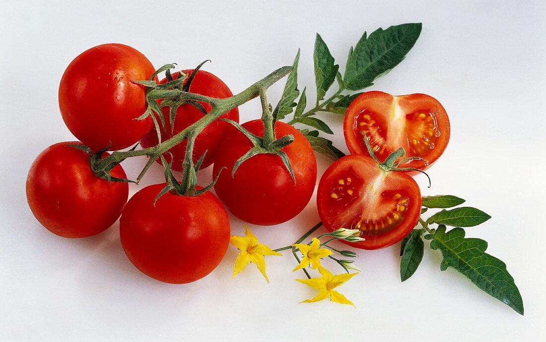 Several vine tomatoes, whole and halved, with leaves and flowers