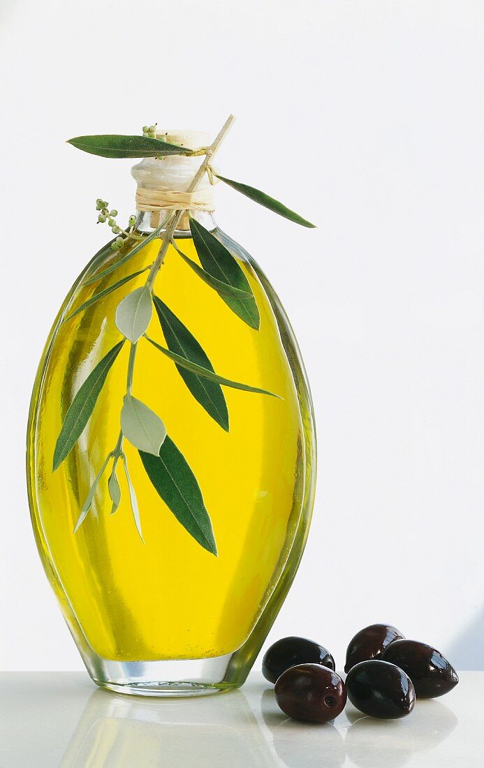 A bottle of olive oil, an olive twig and a few black olives