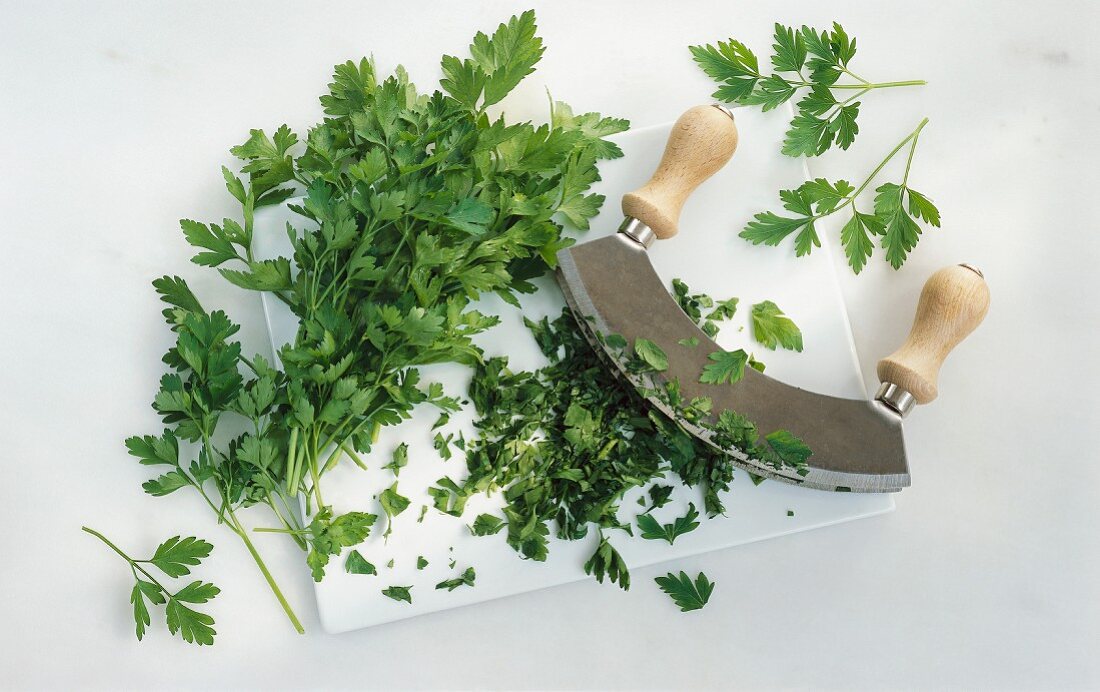 Flat-leaf parsley with a mezzaluna on a chopping board