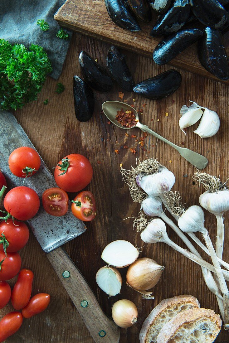 A still life featuring mussels, garlic, onions, tomatoes and parsley