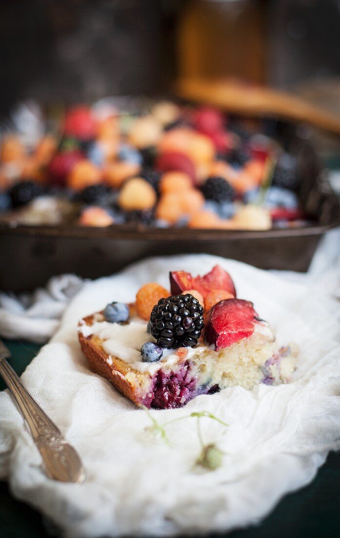Ein Stück Blechkuchen mit Lavendel, Vanilleglasur, frischen Beeren und roten Pflaumen