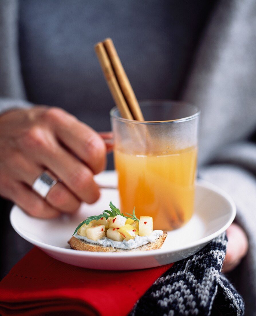 A woman holding a plate with a glass mug of tea and a small slice of bread with topping