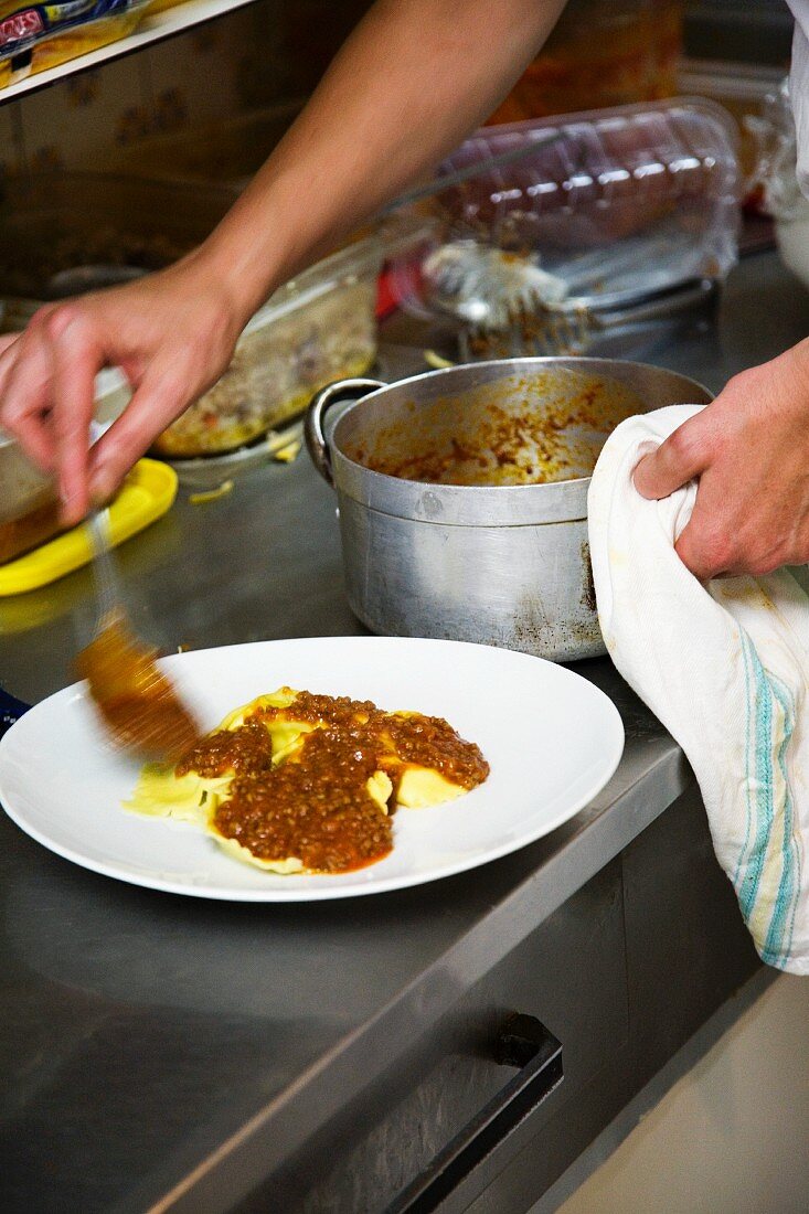 A chef dishing up ravioli and minced meat sauce in a commercial kitchen