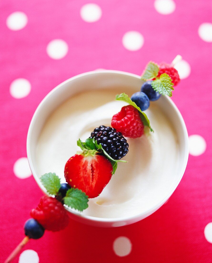 A berry skewer with mint on a bowl of whipped cream