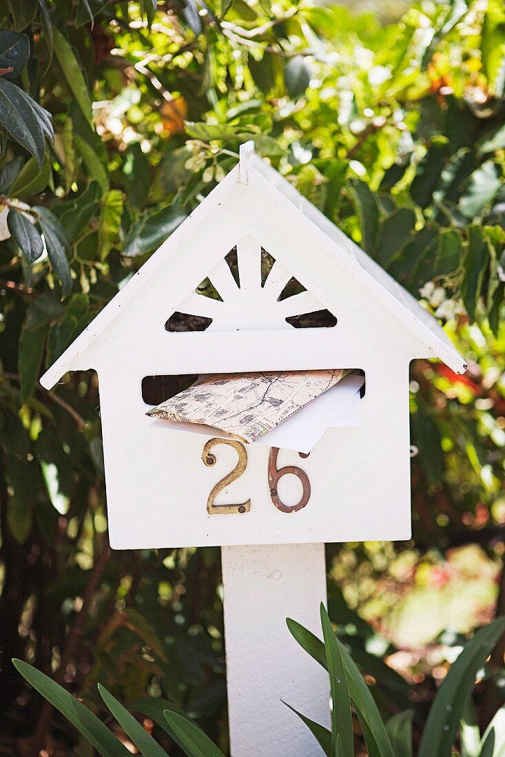 White-painted letter box shaped like a house with house number and white wooden post