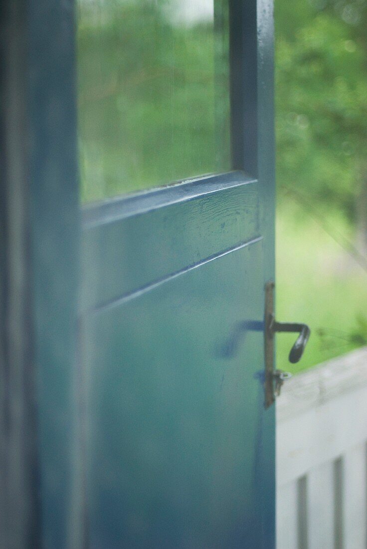 Wooden door painted petrol blue with window pane and simple, black fittings