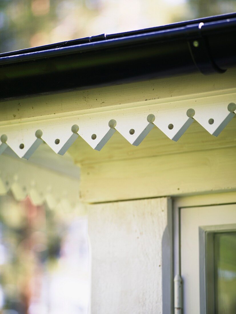 Traditional, white-painted, carved wooden trim on Swedish porch with dark guttering