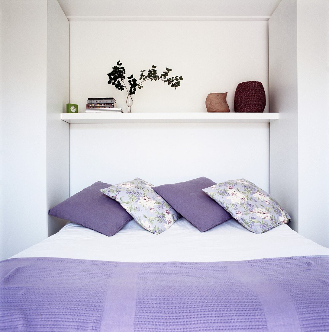 Purple bedspread and scatter cushions on bed with shelf in niche above head
