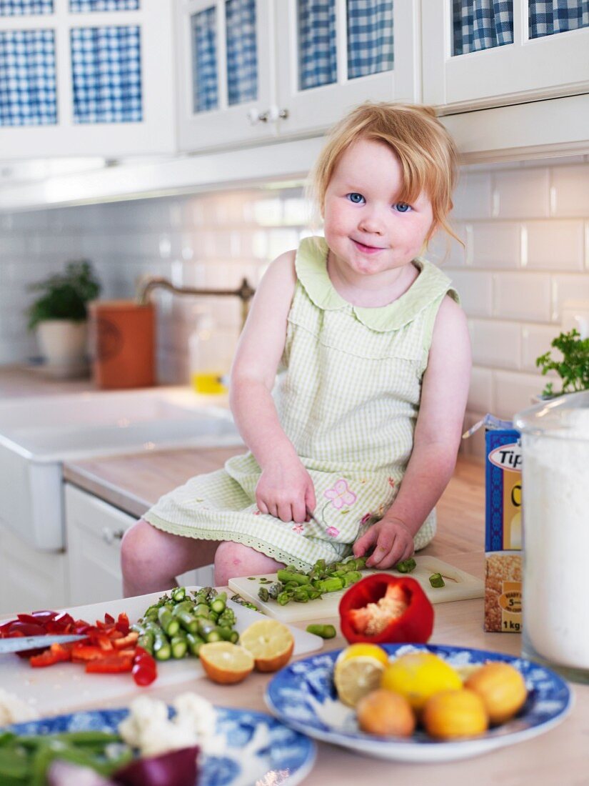 Little girl sitting on kitchen worksurface chopping vegetables