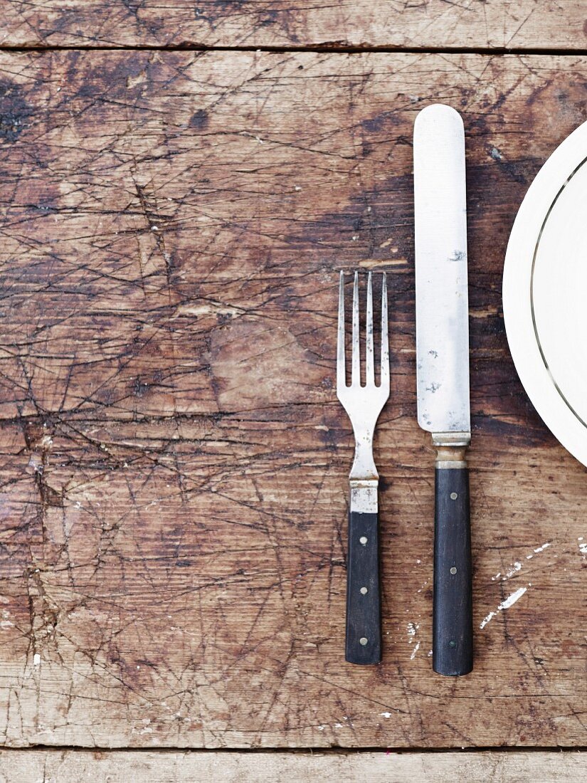 Fork, knife and plate on wooden table, directly above