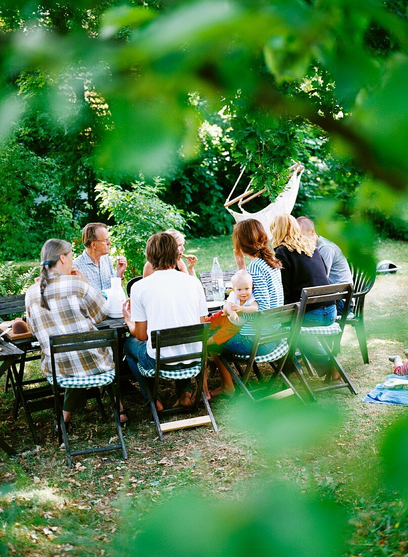 Erwachsene & ein Kleinkind sitzen an gedeckten Gartentisch