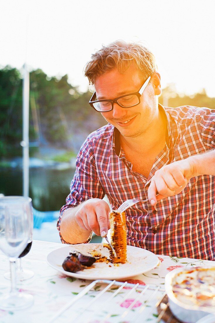 Mann isst gegrillten Maiskolben an Tisch im Freien