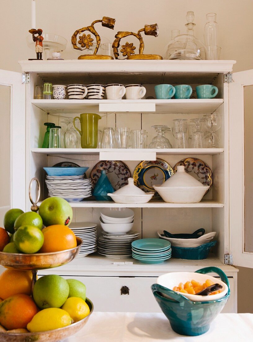Blick in Geschirrschrank auf Tassen und Teller; im Vordergrund Obst-Etagere und Keramikschale