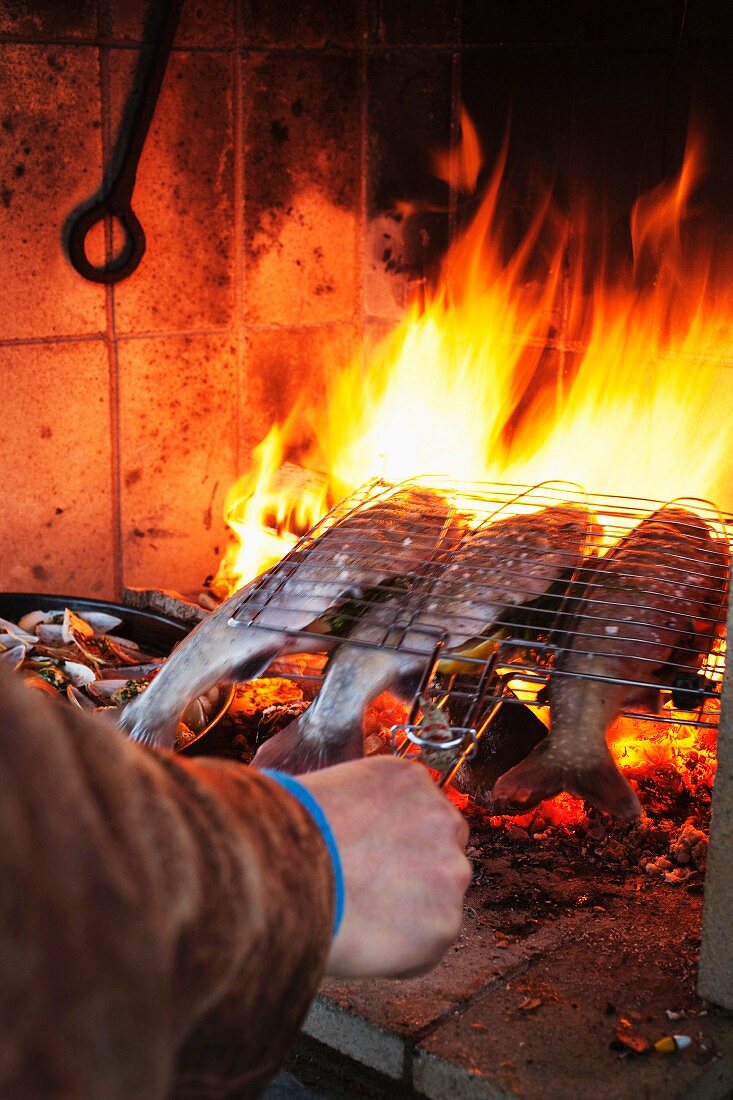 Mann grillt Fische über offenem Feuer