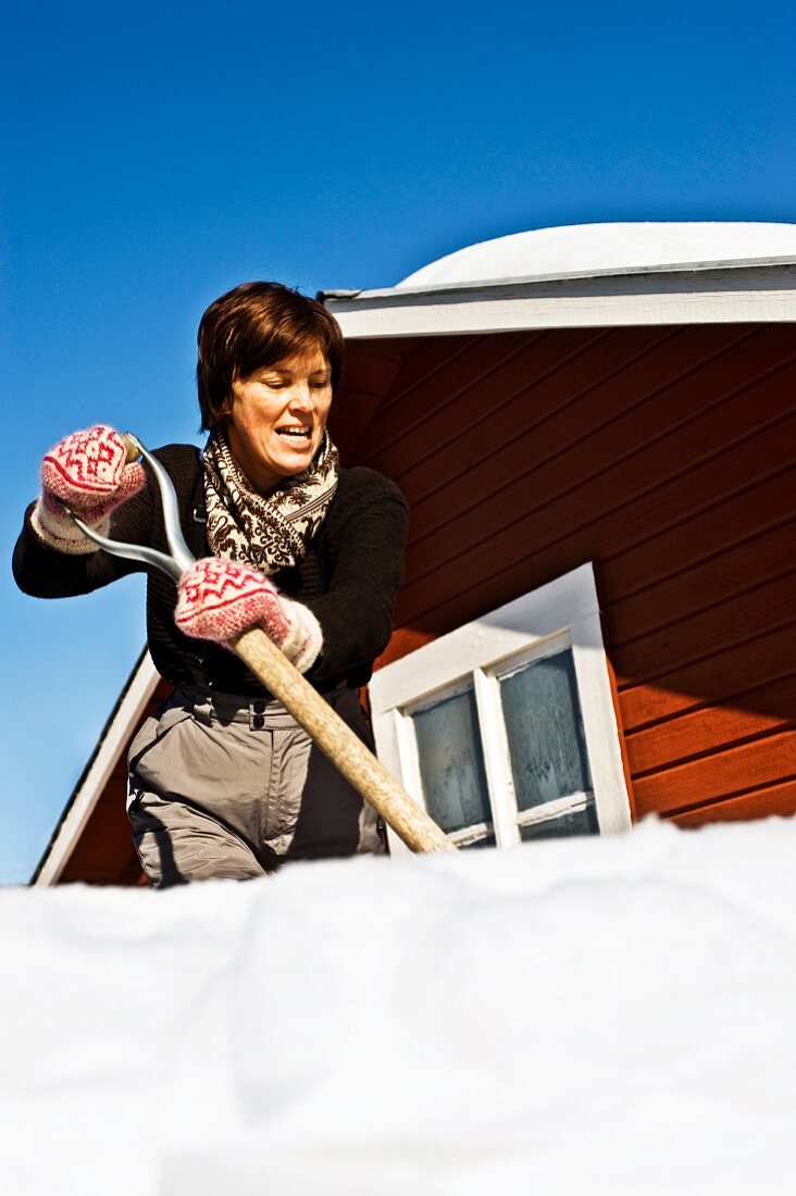 Frau beim Schneeschippen auf dem Dach eines schwedischen Holzhauses