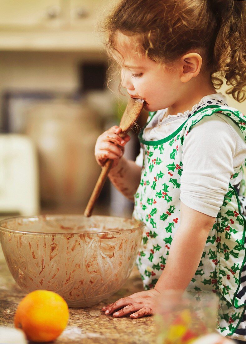Child tasting cake mix with wooden spoon