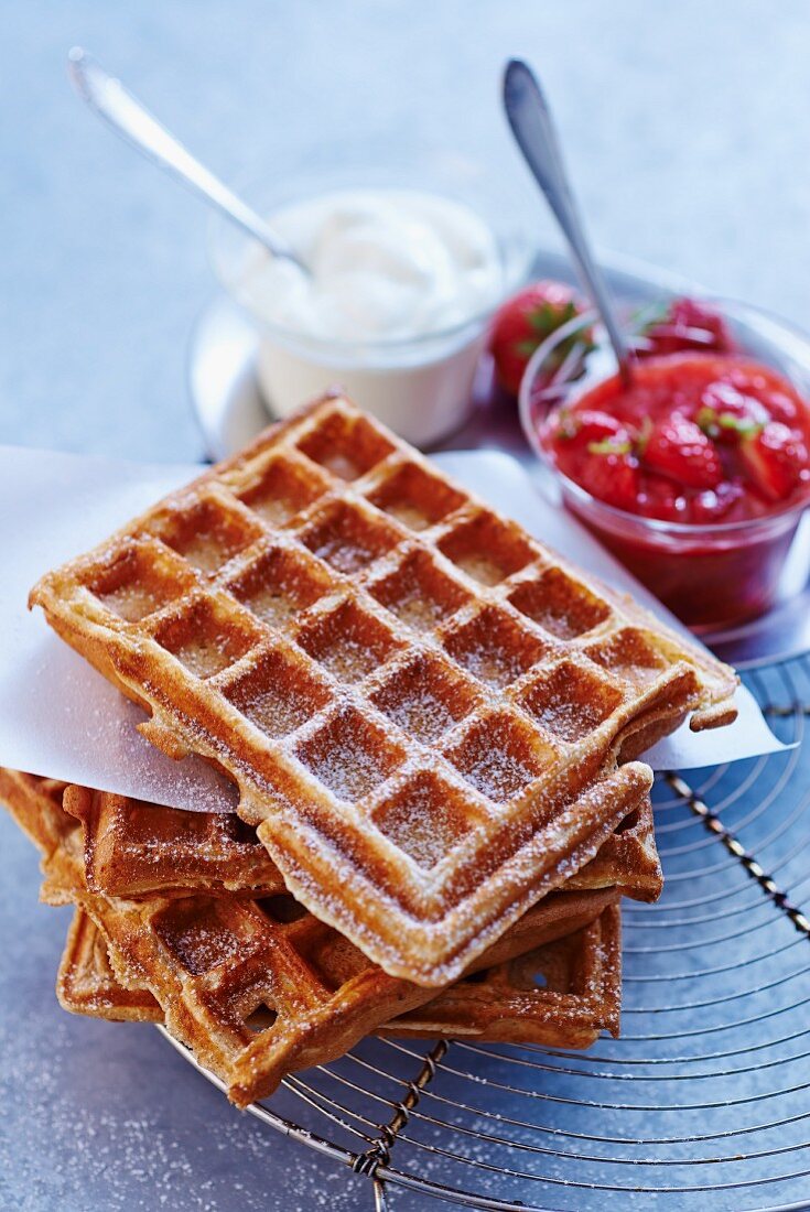 A stack of waffles with icing sugar, strawberry compote and cream