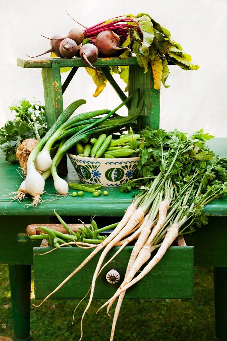 Stillleben mit verschiedenen frischen Gartengemüsen auf altem grünen Tisch, mit geöffneter Schublade, alter Keramikschüssel und Holzmesser