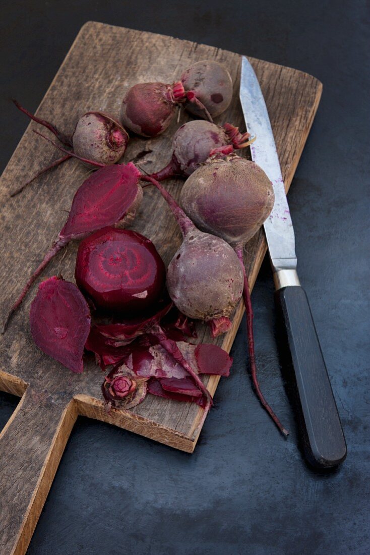 Several boiled beetroot, some peeled, on a wooden board with a knife