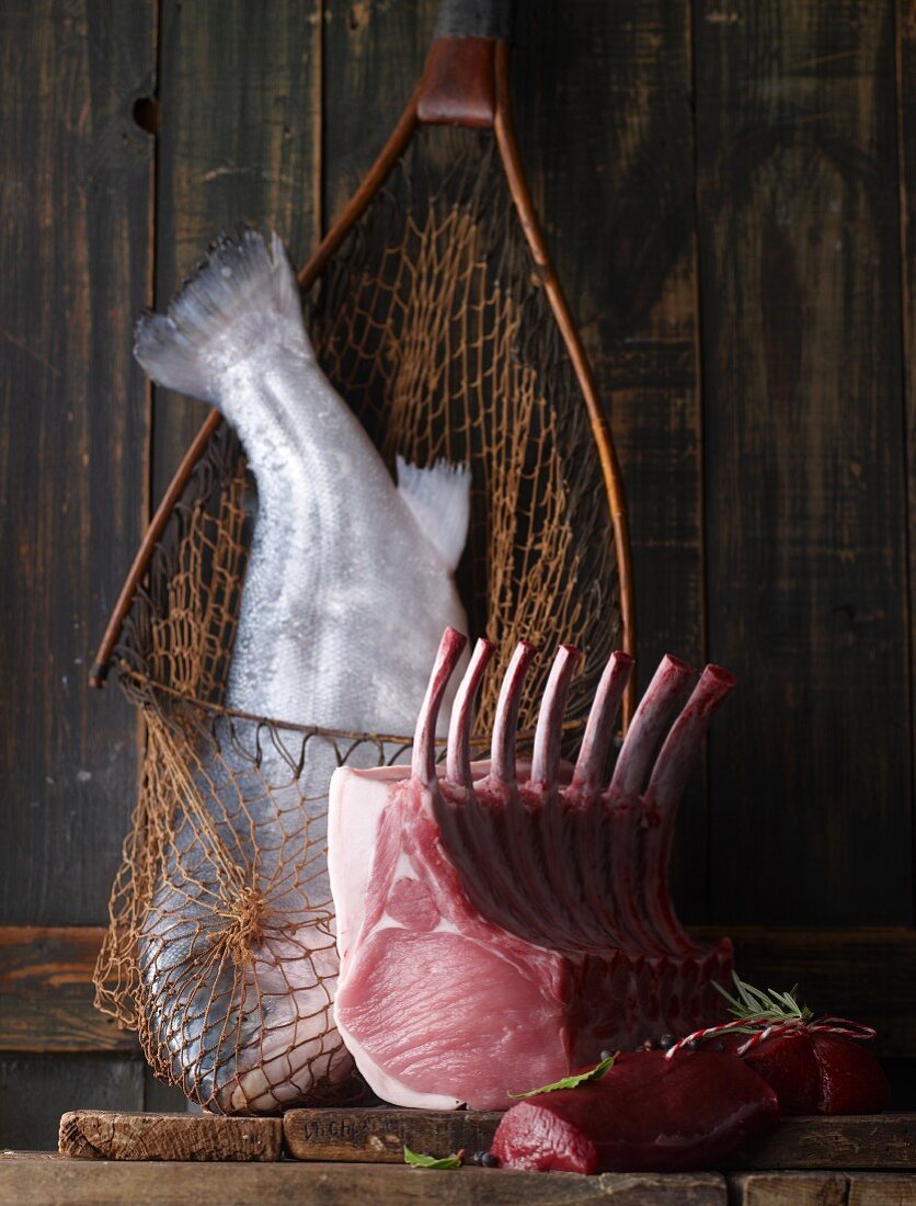 A fishing net with fish, a rack of pork and a venison fillet on a wooden board
