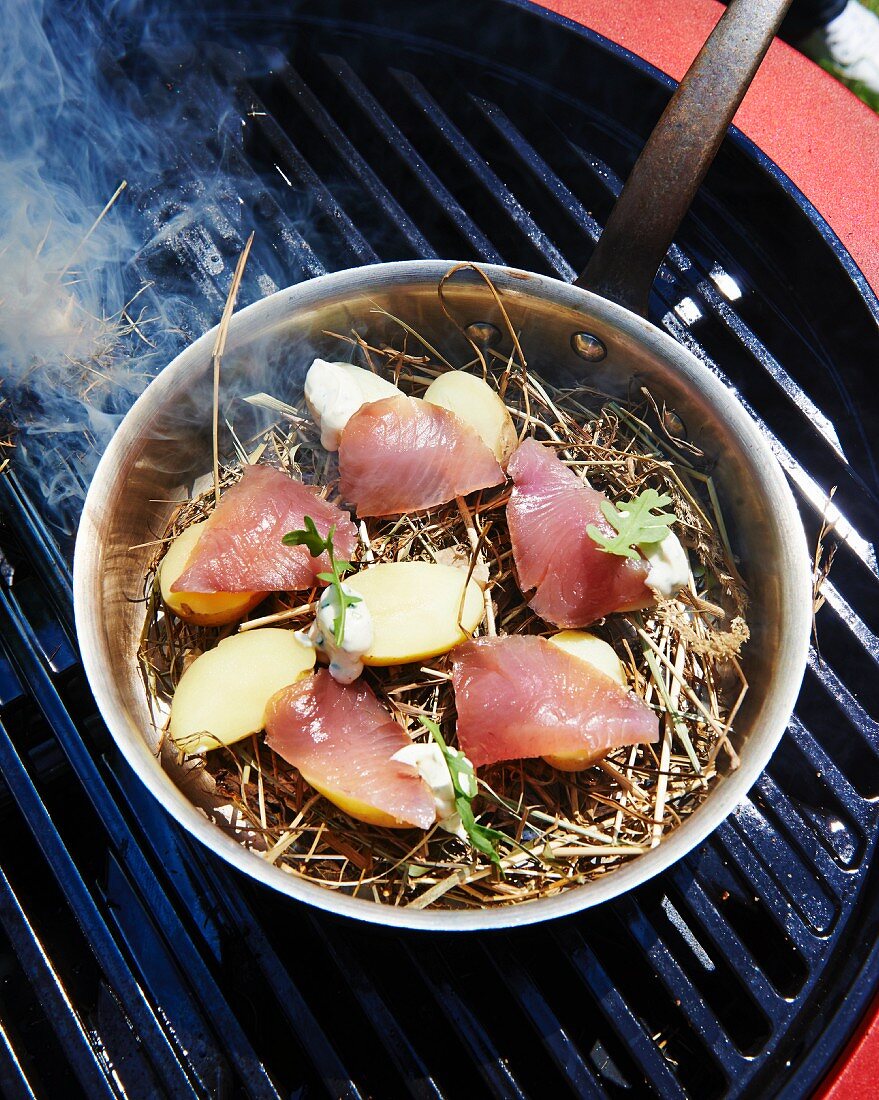 Bonito and potatoes on straw in a pan on a barbecue grate
