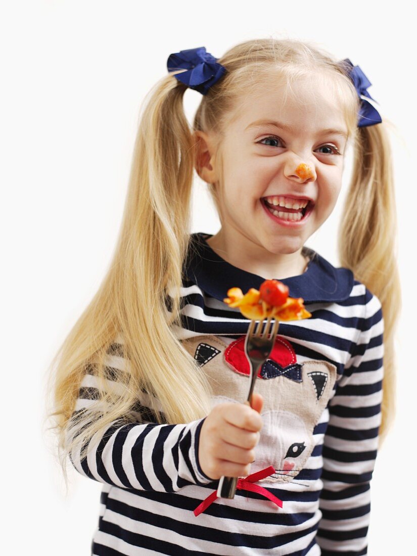 A small girl holding a fork with pasta and tomato