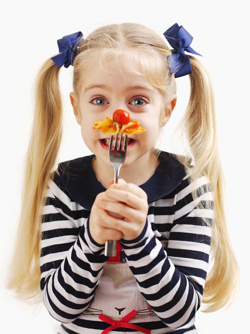A small girl holding a fork with pasta and tomato