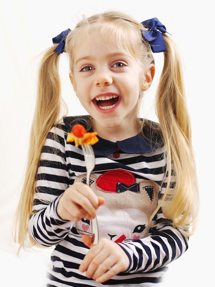 Kleines Mädchen hält eine Gabel mit Nudeln und Tomate