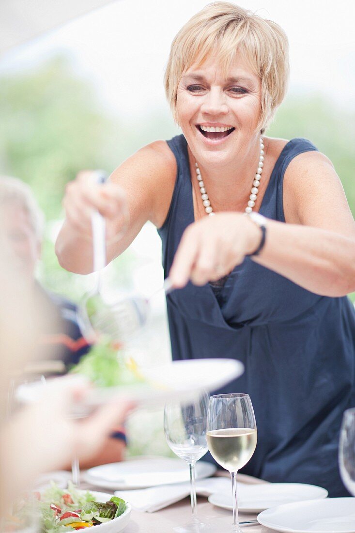 A woman in an elegant dress serving salad at a table outdoors