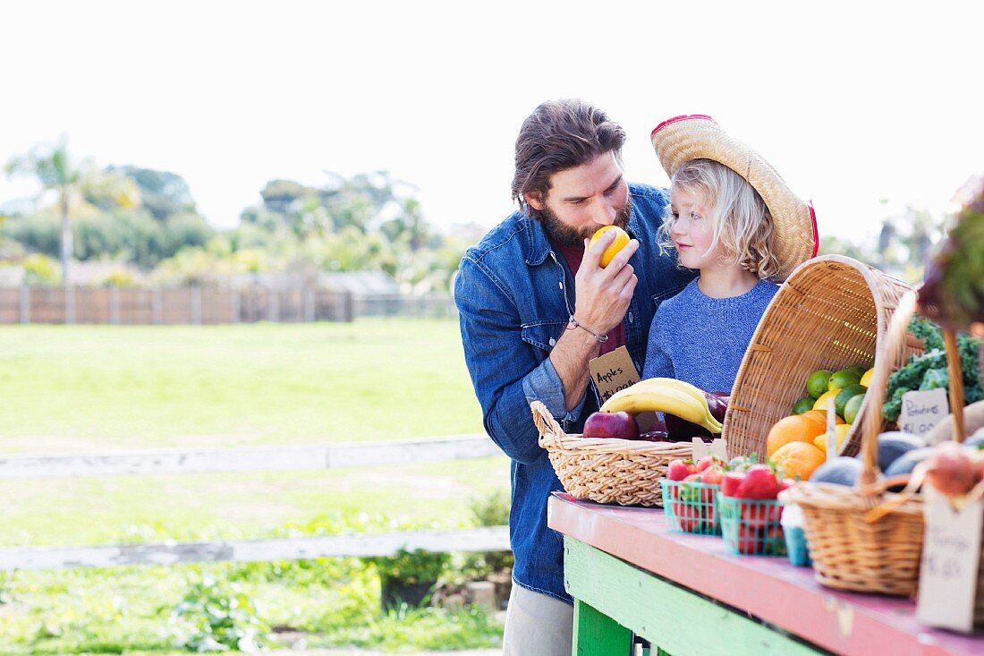 A father and daughter at a stall at a farmer's market with fresh fruit and vegetables