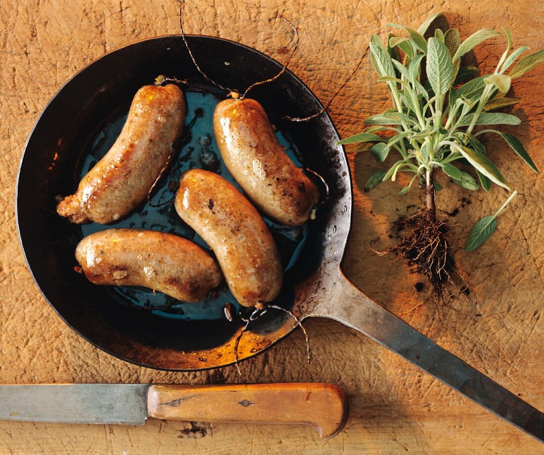 Sausages fried in a pan, and freshly harvested sage