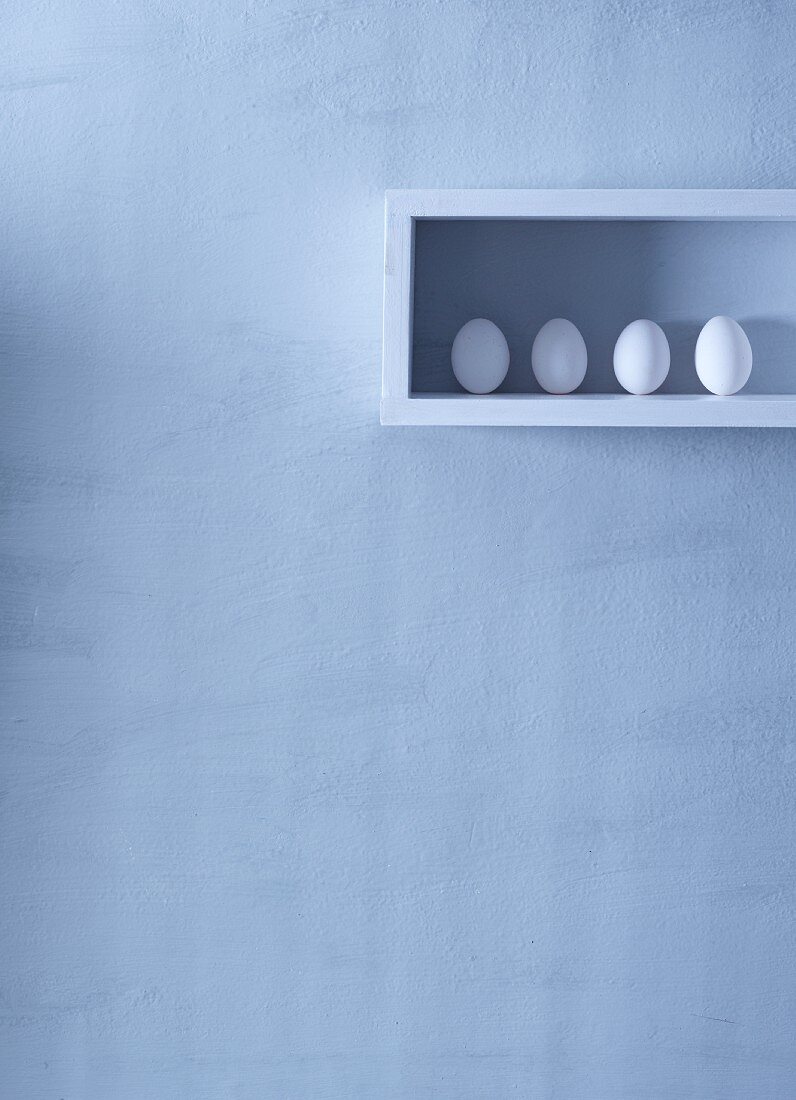 Vier weiße Eier in einem Regal an der Wand