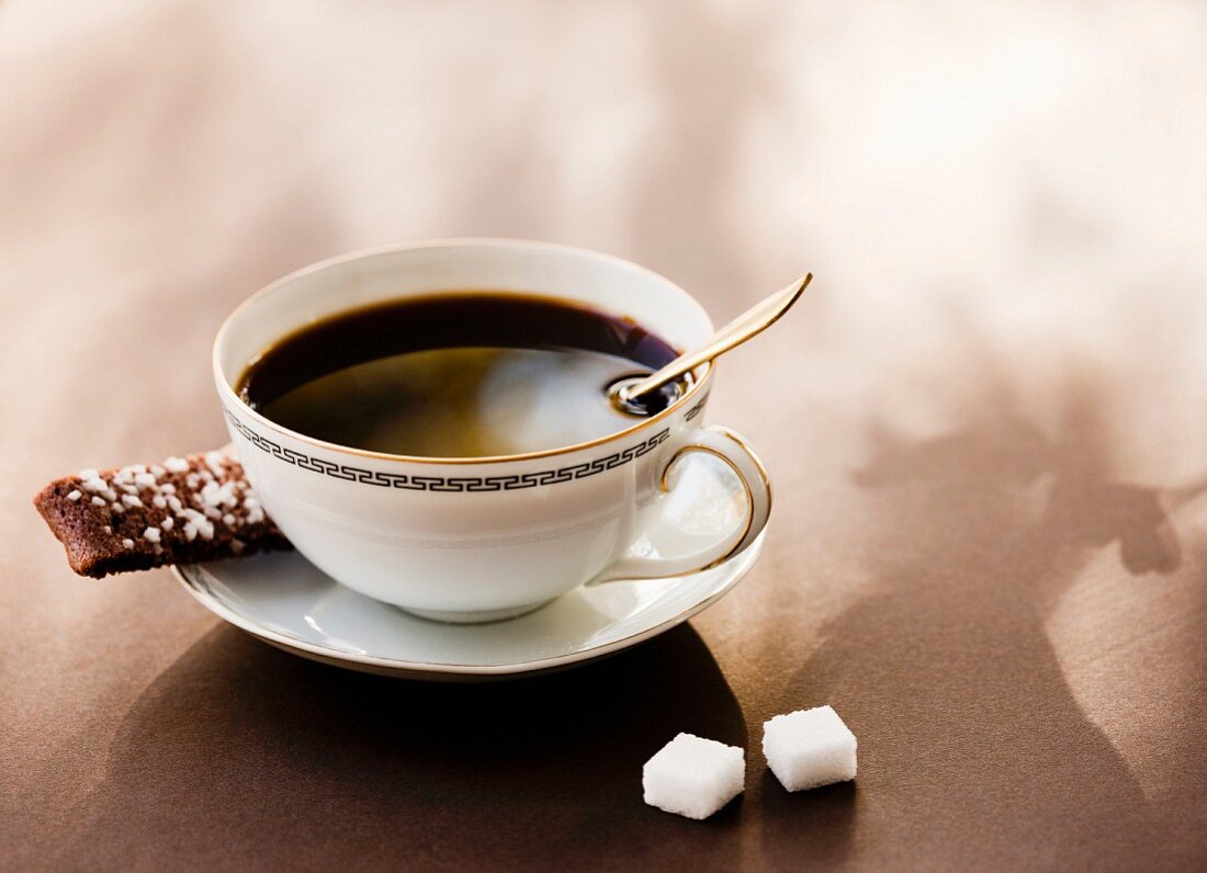 Eine Tasse schwarzer Kaffee mit Kaffeeplätzchen und Würfelzucker