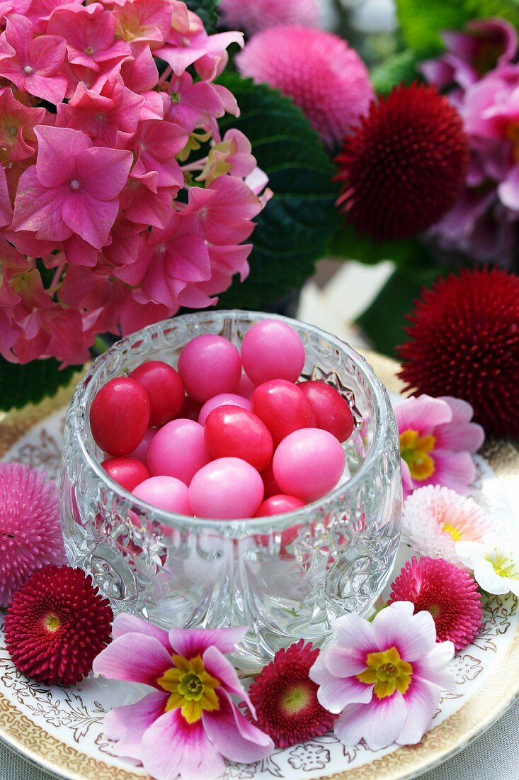 Kristallgefäss mit rosa und pinkfarbenen Zuckereiern umgeben von Frühlingsblüten