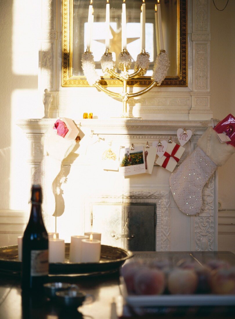 Bottle and lit candle on table, mantelpiece with Christmas decorations and brass candlestick in front of mirror