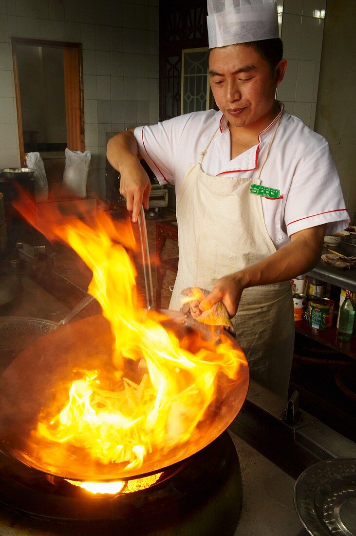 Chinesischer Koch mit brennendem Öl im Wok