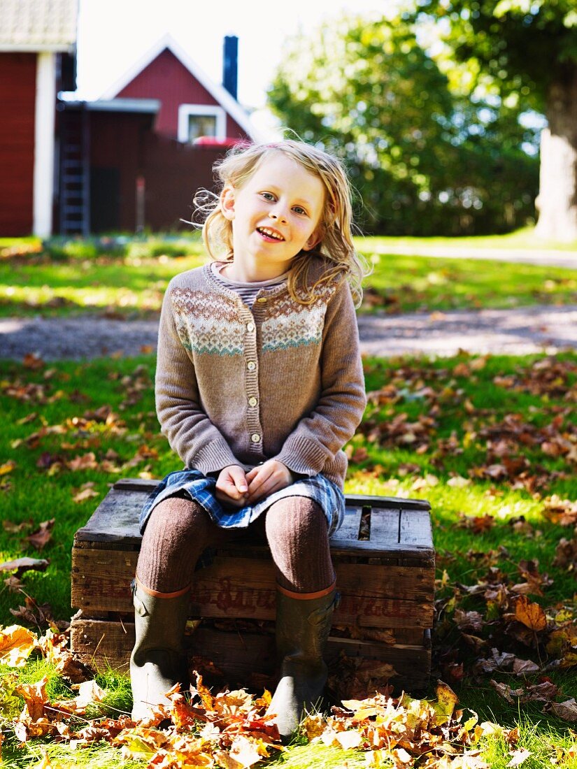 Mädchen sitzt auf Holzkiste in herbstlichem Garten