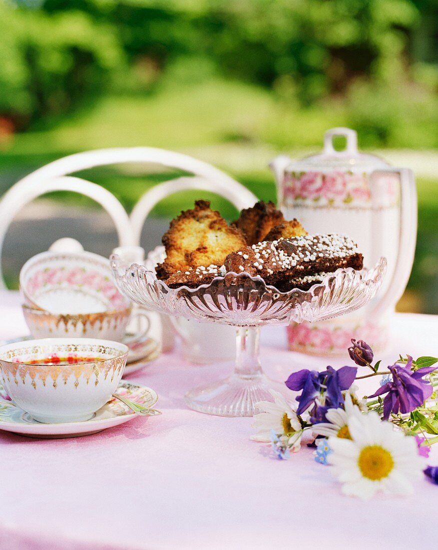 A table outdoors with teacups and cakes in a decorative serving dish