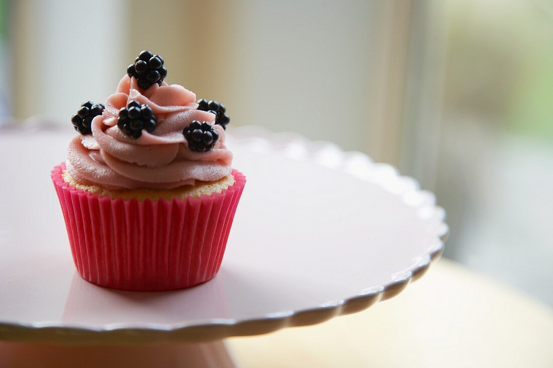 Cupcake topped with blackberries, on a cake stand